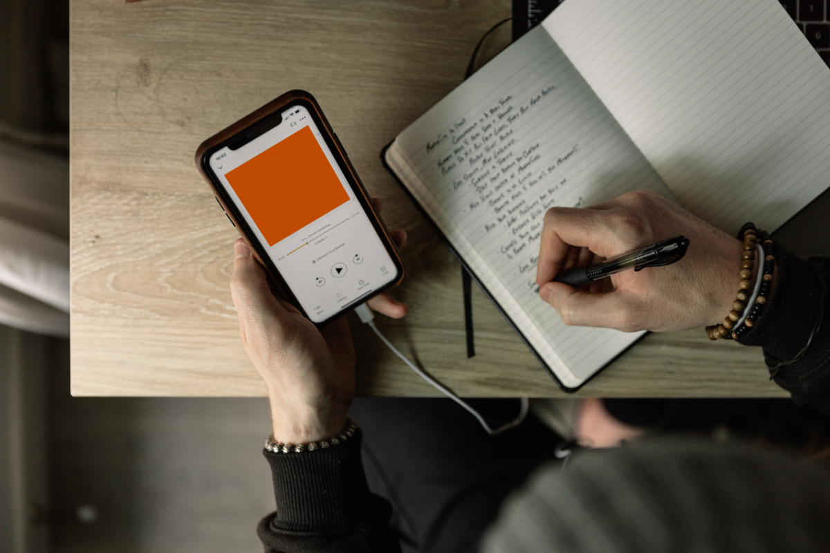  A person is seen taking notes while listening to a podcast on their smartphone.