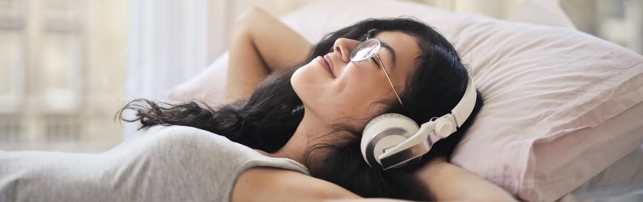 woman listening to music with headphones on in the bed