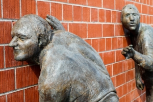 two statues listening behind a wall