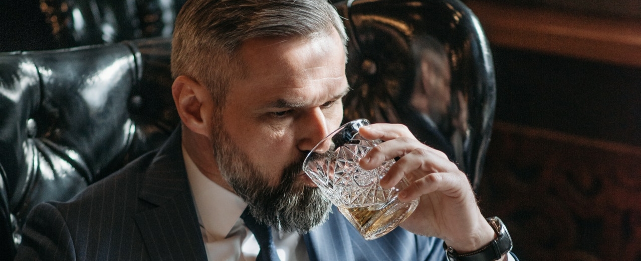 bearded man in a suit drinking a glass of whisky