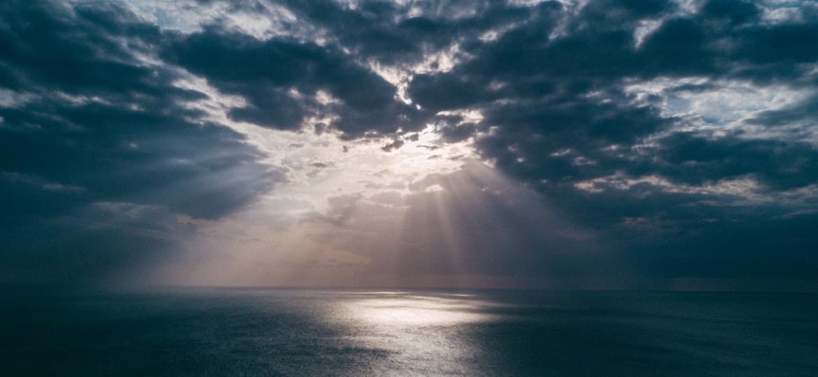 the sun coming out of a cloudy sky on top of the ocean